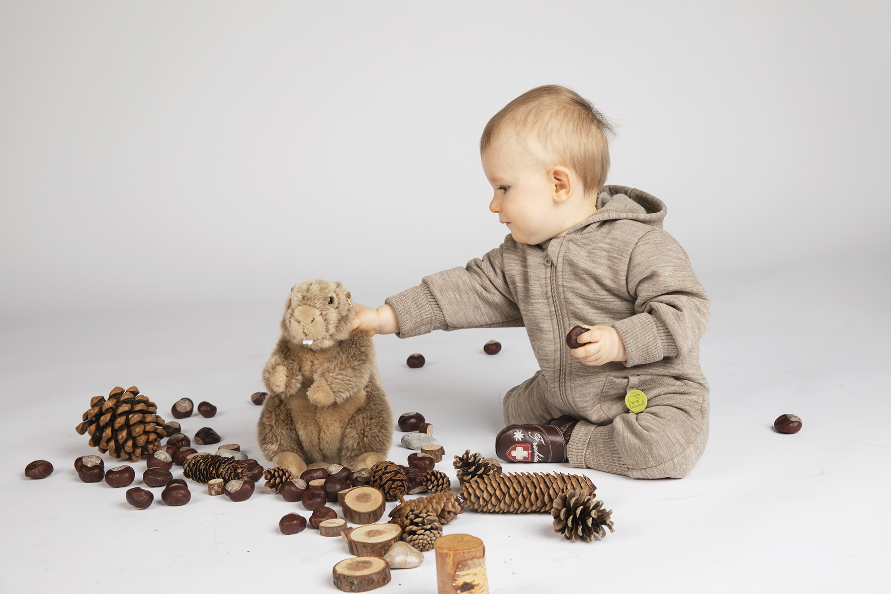Baby, sitzend mit Biber-Kuscheltier und verschiedenen Tannenzapfen spielend
