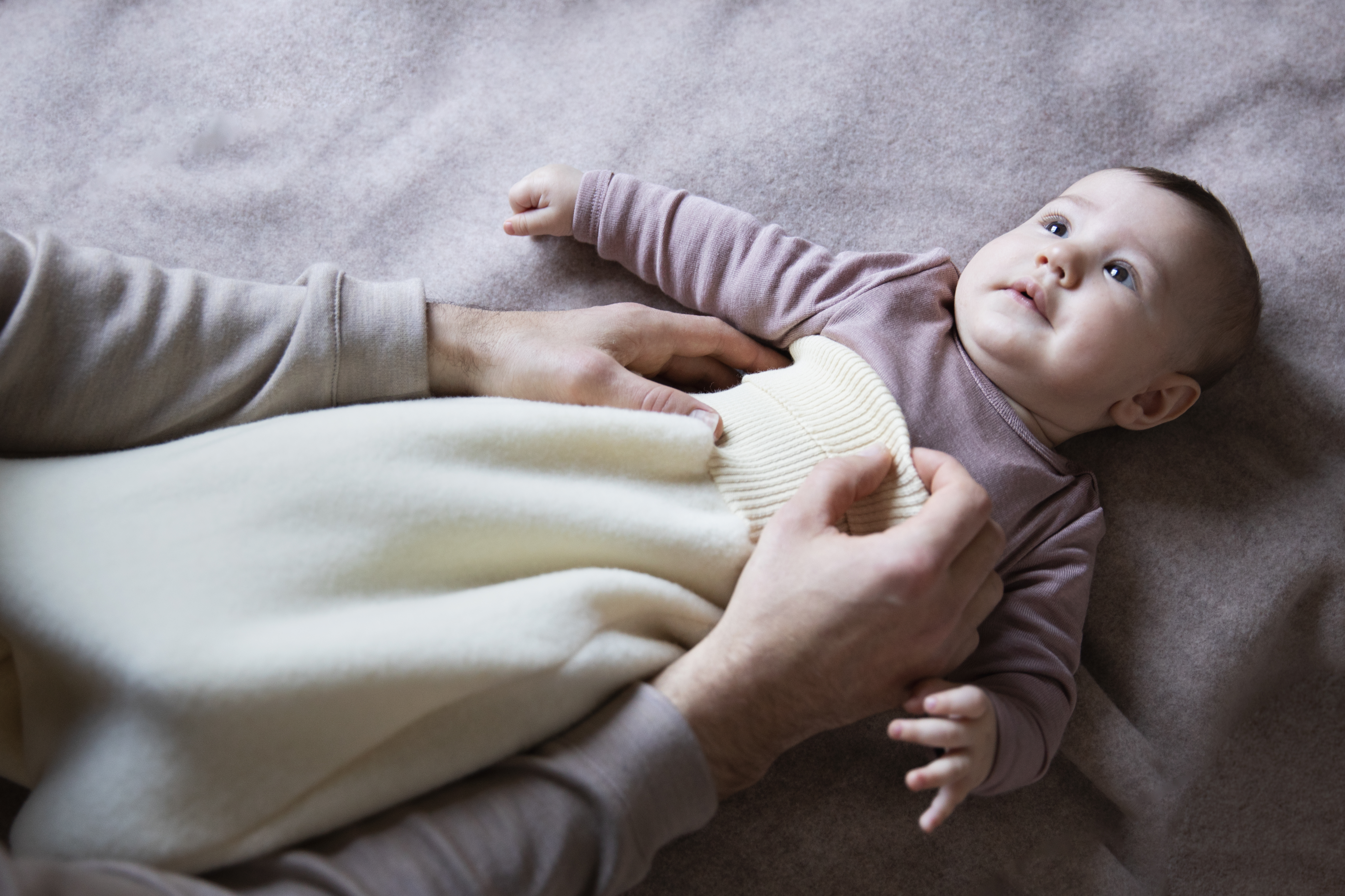 Baby being dressed by dad in an ENGEL merino wool sleeping bag.