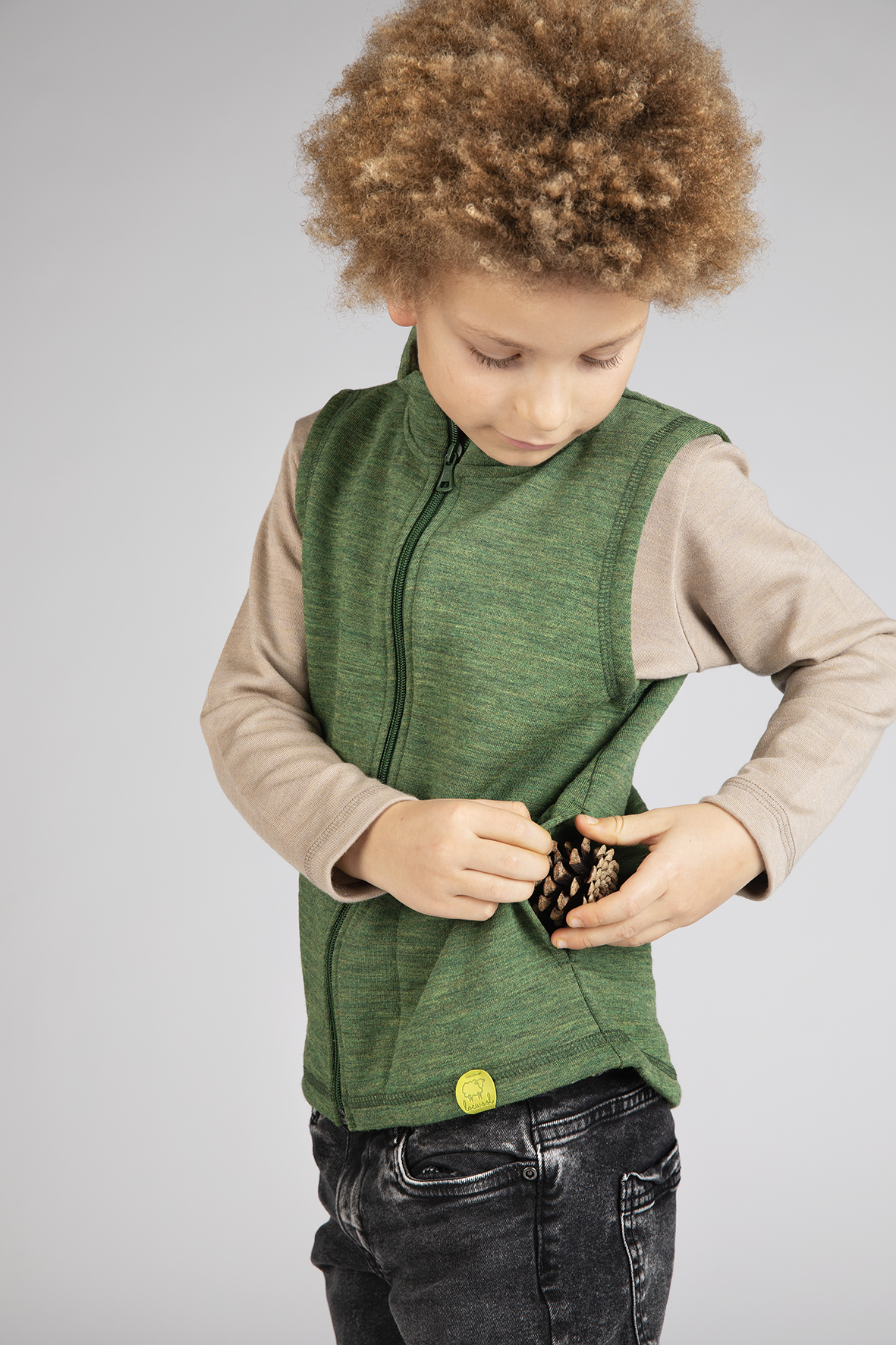 Kind trägt Engel Weste aus süddeutscher Merinowolle und steckt einen Tannenzapfen in die Jackentasche