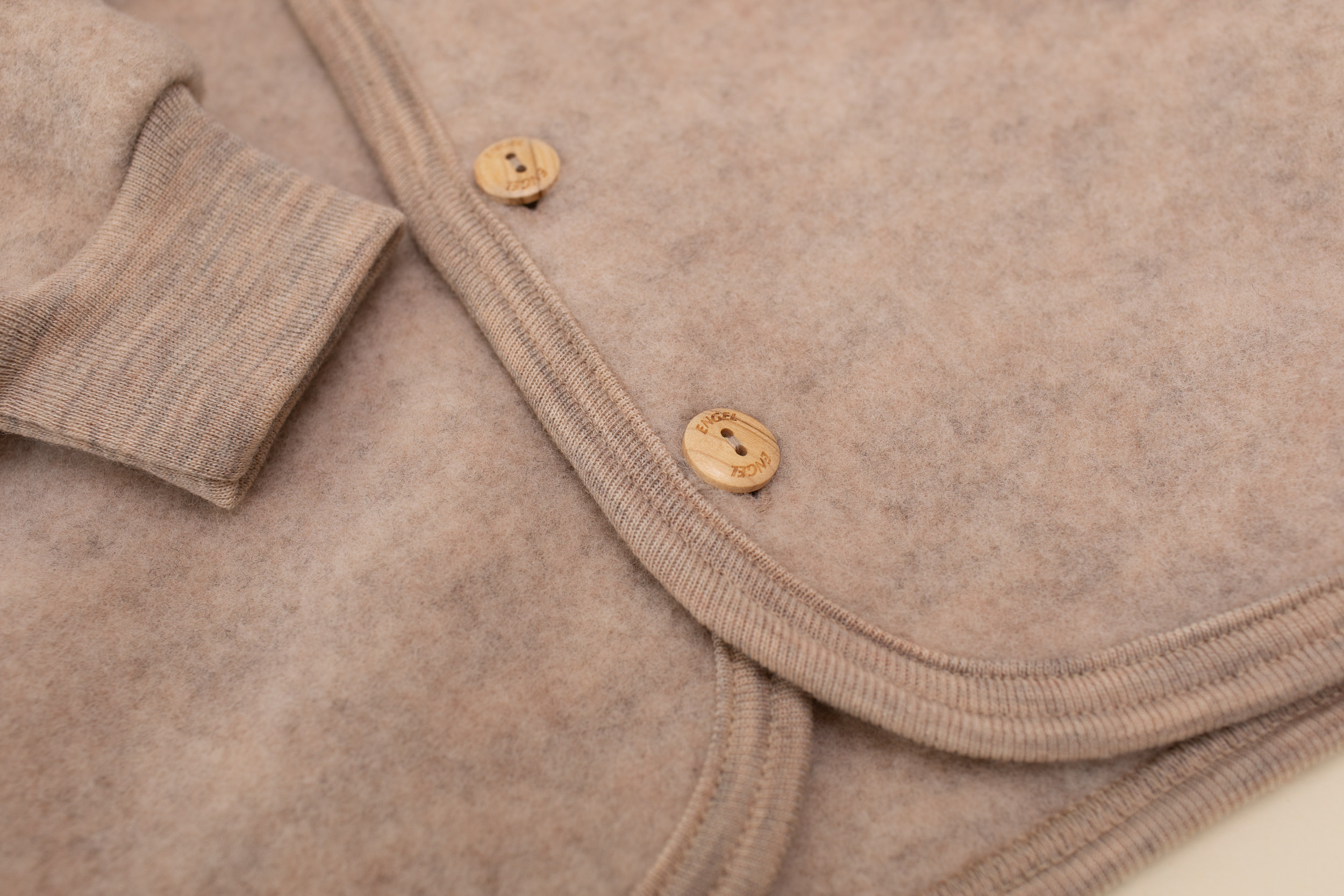 Detail shot of a sand-colored wool fleece baby jacket by Engel with wooden buttons.