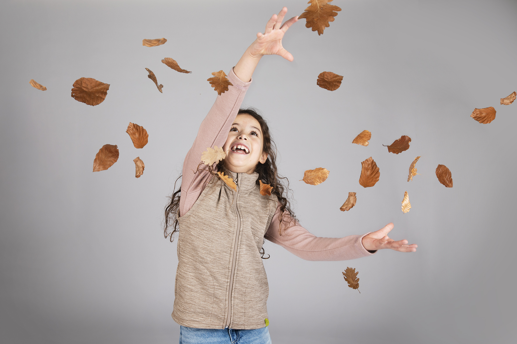Kind trägt eine Engel locwool Weste aus regionaler Schurwolle und wirft fröhlich Herbstblätter in die Luft.