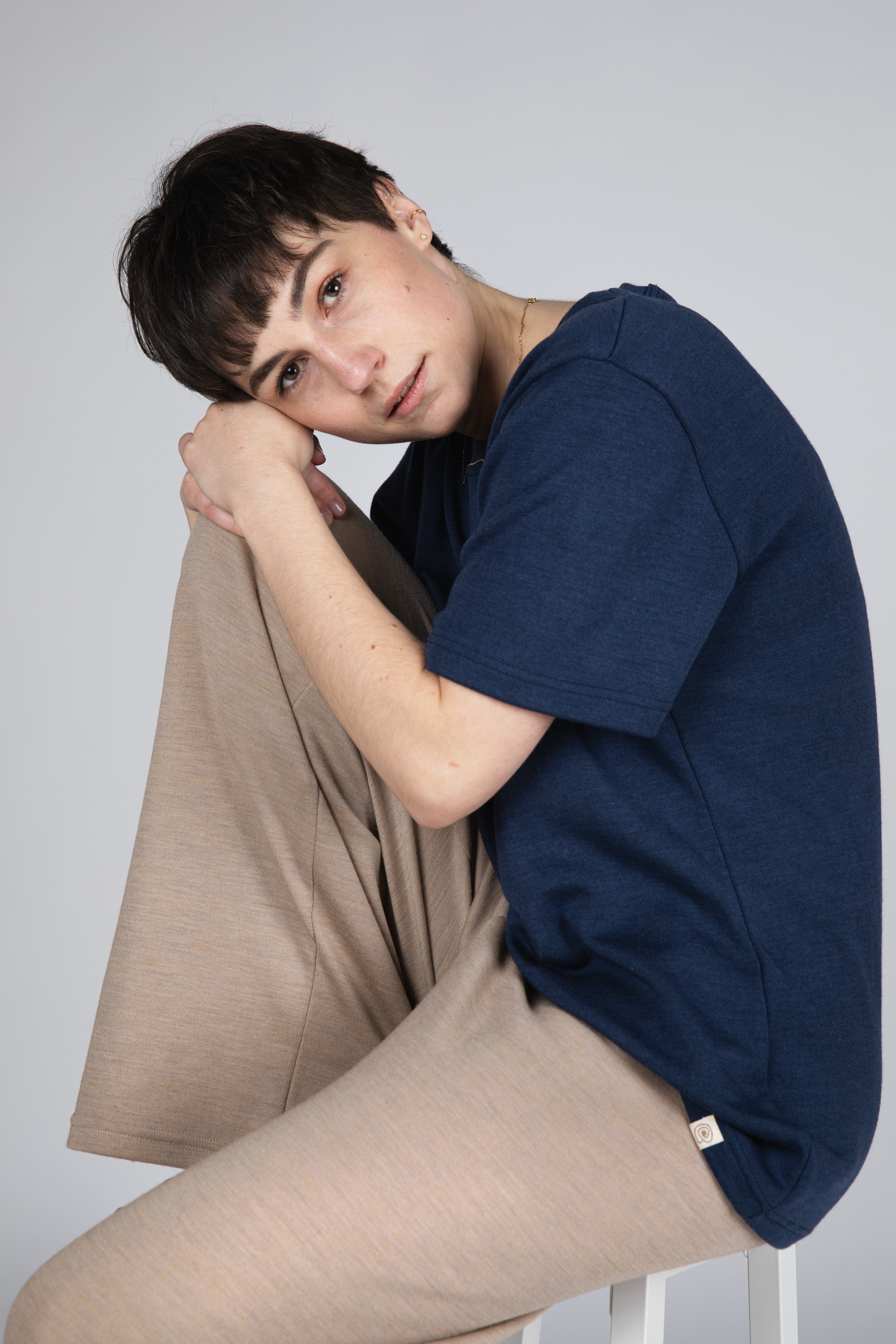 Frau trägt dunkelblaues T-Shirt und beige Wolle-Seide-Interlock Hose von Engel, sitzt entspannt auf einem Hocker vor hellem Hintergrund.