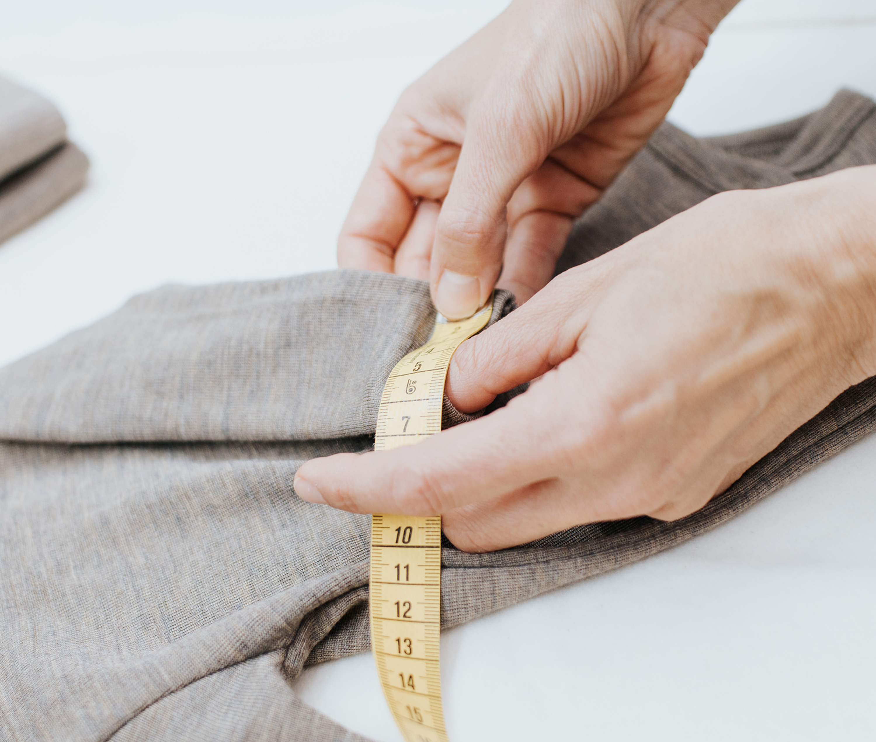Hands measuring a wool-silk baby bodysuit from Engel with a yellow measuring tape.