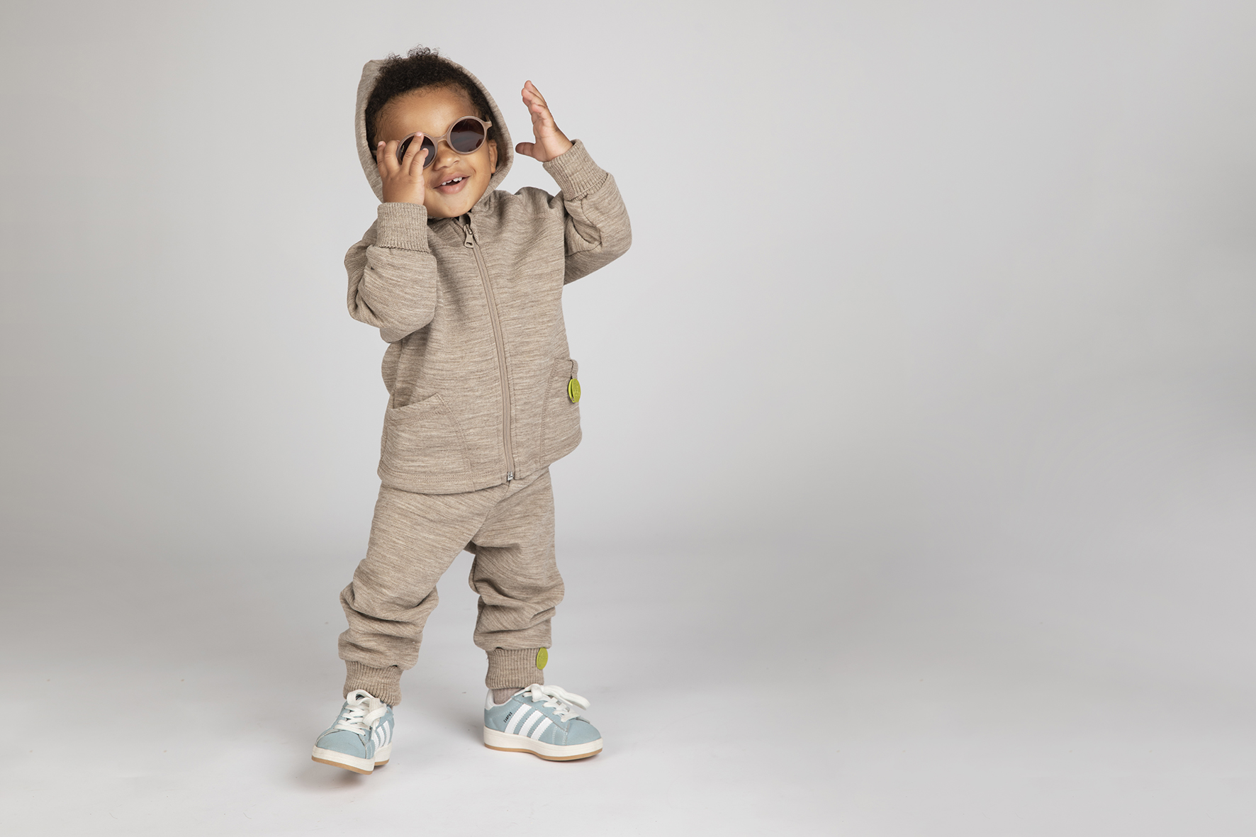 Kind in locwool gekleidet, stehend und lachend mit Sonnebrille